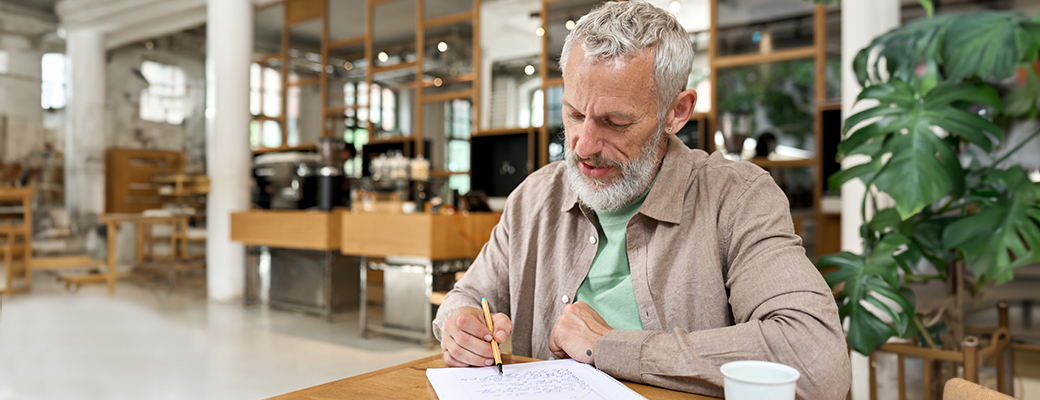 Image of senior man writing at a cafe